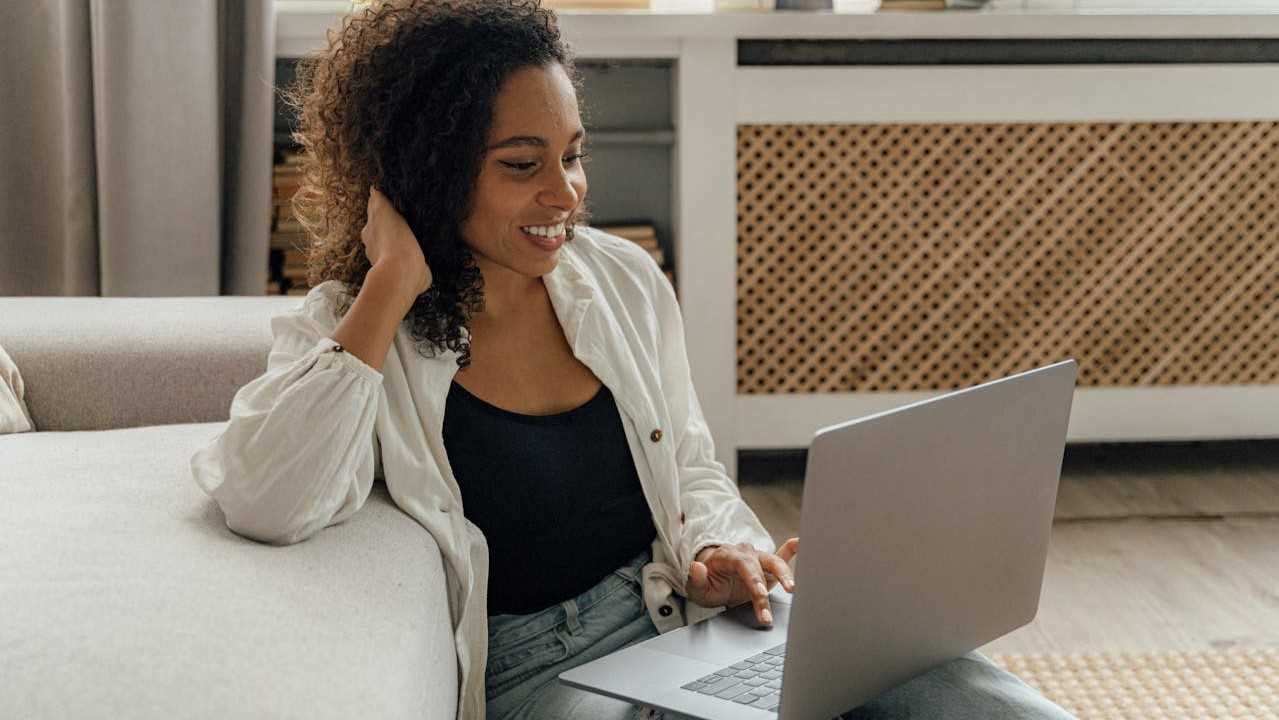 happy girl sitting sitting on floor by couch using computer-shkrabaanthony